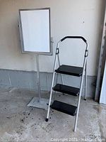 Metal sign holder standing next to the three-step ladder on a concrete floor