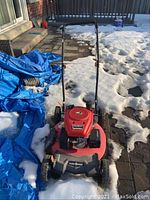 Full front-left view of the red Powersmart lawn mower partially on snow, showing the handle and wheels.