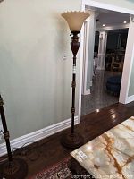 Full view of tall floor lamp with wooden and metal base and amber fluted glass shade, standing against wall