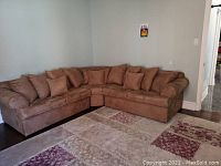 Brown fabric sectional couch with several large and small cushions arranged on dark wood floor with patterned area rug
