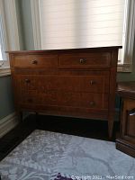 Front view of wooden dresser showing four drawers with metal handles, natural wood finish, decorative veneer/inlay details, and scratches on surface.