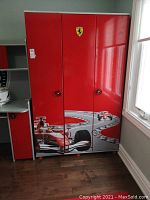 Front view of red Ferrari branded wooden dresser with three doors, displaying Ferrari emblem and racing car graphics.