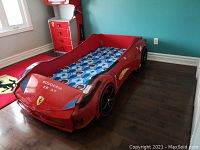 Full view of red Ferrari car bed and mattress against teal wall