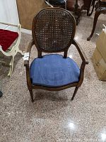 Front view of the wooden chair with armrests and wicker back, showing the attached blue cushion on the seat.