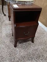 Full view of wooden side table, showing open storage compartment above door and smooth top surface.
