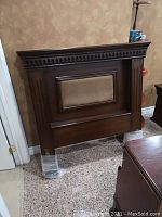 Full view of wooden headboard with fabric center panel and carved details installed on plastic protectors.