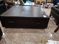 Square wooden coffee table covered in brown faux leather with two drawers, shown from front on granite floor.