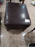 Top view of square wooden ottoman with dark brown faux leather cover showing surface wear and scratches.
