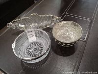 Photo showing three decorative bowls on a dark surface: elongated scalloped clear bowl, clear crystal bowl with swirl bottom pattern, and smaller metallic polka dot bowl.