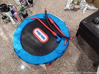 Children's trampoline base with blue padded edges and Little Tikes logo on jumping surface, shown folded with some disassembled bars on top.
