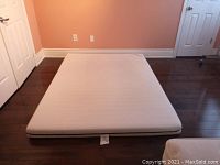 Top down image of the flat queen size mattress laid on dark hardwood floor against a peach colored wall.