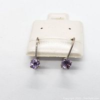 Photo of a pair of sterling silver drop earrings with round amethyst gemstones on a white card stamped Sterling Silver.