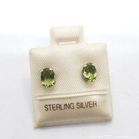 Pair of genuine peridot oval stone earrings set in sterling silver shown on a white display card labeled 'Sterling Silver'.