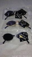 Three pairs of Daya brand small oval sunglasses with tags, sealed in plastic, showing frames and lenses.