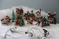 Photo showing all ten Christmas village pieces arranged on a white surface with a light string in foreground.