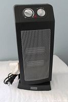 Photo of a black Classic oscillating heater model 3836-525 with metal mesh front, two control knobs on top right side, and attached power cord.