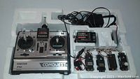Silver and black Futaba Conquest FP-T6NFK radio control transmitter with two joysticks, FM receiver labeled FP-R701, four different sized servos with wires, and a power adapter, all set in a white molded foam tray.