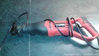 Full view of the reciprocating saw showing red and black housing, ergonomic handle, power cord, and blade.