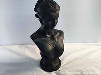 Front and angled view of a black matte bust statue of a woman used for jewelry display, wearing a delicate gold-tone chain necklace with a small pendant