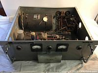 Front and internal view of the rack mount power supply showing analog meters, internal rotary components, and metal housing with handles.