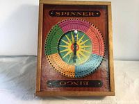Full photo of the wooden carrying case with vintage bingo spinner mounted on the lid. Shows the overall item and spinner layout.