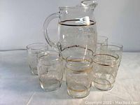 Vintage glassware set with carafe and six glasses, all featuring etched floral patterns and gold rims.