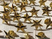 Close-up of gold star pin badges showing the textured five-pointed star design and clutch backs.