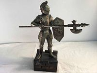 Full front view of bronze-colored metal medieval knight figurine holding spear and shield on wood base.