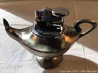 Side and front view of the vintage Aladdin genie lamp table lighter showing copper and chrome finish and lighter mechanism.