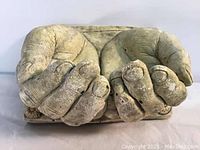 Front view of large handcrafted clay hands sculpture shaped to form a bowl, showing realistic detailed fingers and nails with natural-aged clay finish and some surface wear.