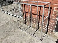 Photo of one aluminum welded square tube frame shelving unit standing outdoors against a brick wall, showing its height and open side design.