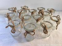 Front view showing all 14 clear glass tea candle holders arranged in clusters, each with a rustic twine bow tied near the top.