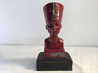 Front view of the red and black painted steel bust statue of Egyptian Queen Nefertiti on a black base showing some paint peeling.