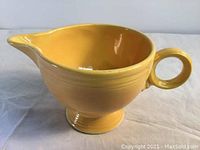 Yellow ceramic creamer with round ring handle and visible chip at the lip edge.