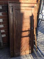 Full view of vintage wooden cabinet door with frame leaning against brick wall outdoors, showing door, attached frame, and positioning of glass handle.