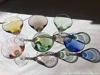 Top view of seven colorful wine glasses arranged in sunlight showing their colors and shadows.