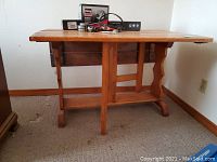 Front view of the table showing solid pine construction, gate leg supports, and table surface with items on it.