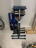 Two new Mastercraft 3-in-1 workpiece support stands in original blue boxes next to four used blue metal shop support stands with adjustable arms and rubber feet.