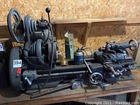 Front and left side view of lathe showing pulley drive, spindle, and handwheels on wooden shelf