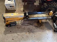 Full side view of yellow log splitter on garage floor showing overall length, beam, wedge and wheels