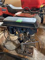 Front angle showing drill press base, work table with two large bits, and motor housing on top.