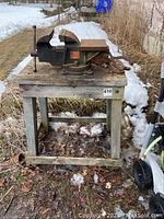 Front view of bench vise mounted on wooden stand outdoors with snow and grass in background