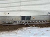 Full length view of aluminum two-section extension ladder lying on ground against siding