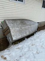 Boat hull exterior resting upside down against siding in snow