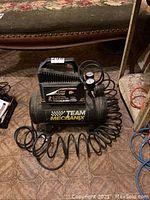 Full view of Team Mechanix air compressor with hose and nozzle on carpeted floor near furniture.