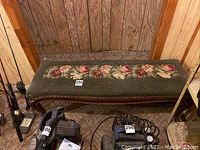 Top and angled views of vintage wooden bench with floral needlepoint upholstery showing wear and damage to fabric as well as carved Queen Anne legs.