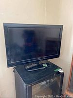 Wide view of Dynex 31 inch television with pedestal stand and remote on top of a black cabinet.