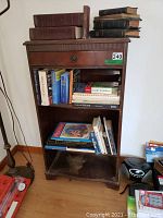 Front view of small wooden bookshelf with books on shelves and top, showing dovetailed drawer and wear.