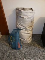 Rolled deflated off-white vinyl inflatable boat standing next to blue mesh bag containing pump and hoses.