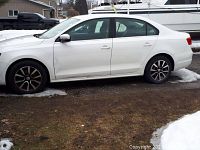 Driver side profile of white Jetta showing alloy wheels, door panels and minor rust at wheel wells.